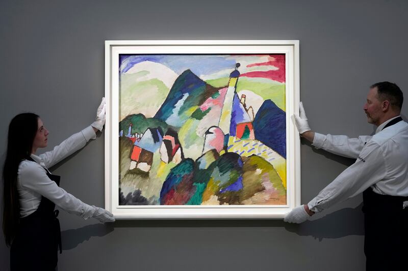 Members of staff hold the painting “Murnau with Church II” by Wassily Kandinsky during a media preview of Sotheby’s auction in London.