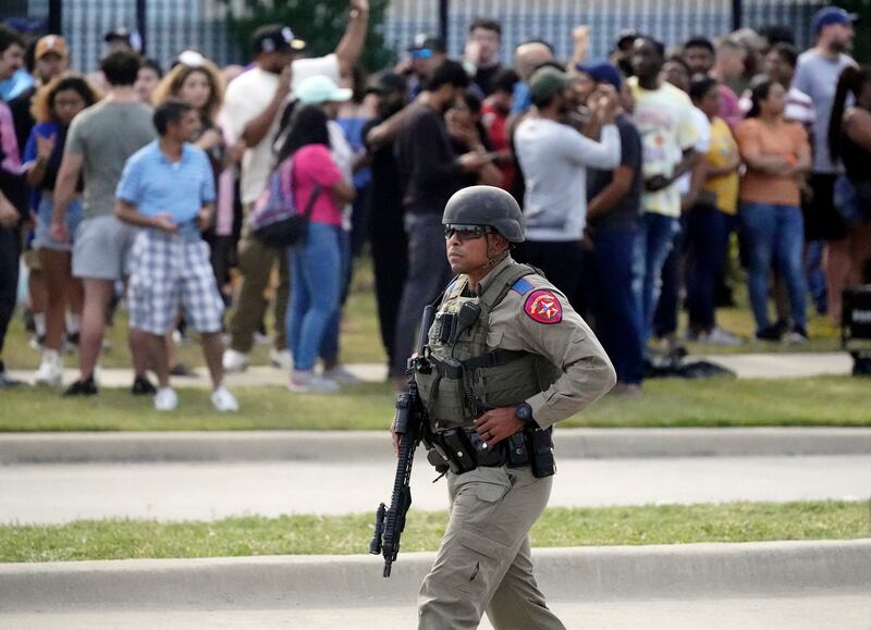 A law enforcement officer walks as people are evacuated from a shopping center where a shooting occurred, in Allen, Texas.