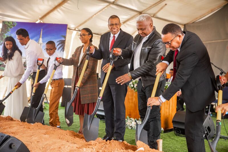 A line of people in Sunday best holding shovels into the dirt.