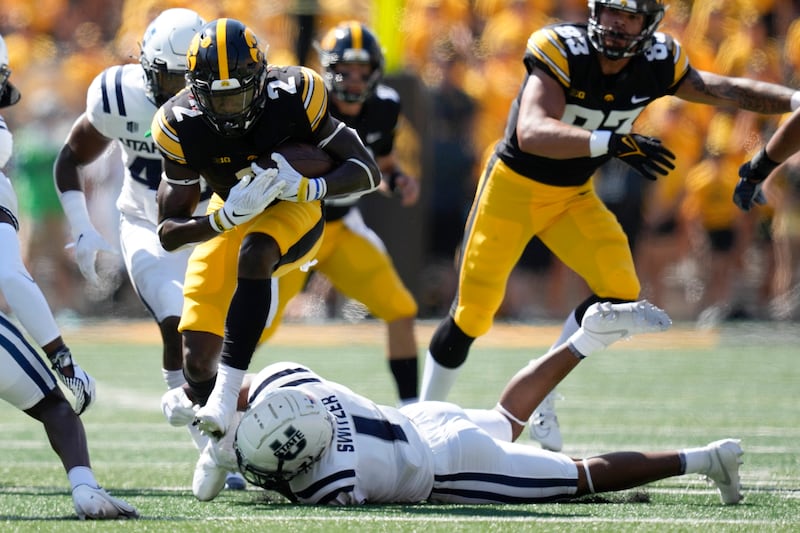 Iowa running back Kaleb Johnson (wearing black) tries to break a tackle by Utah State safety Anthony Switze.