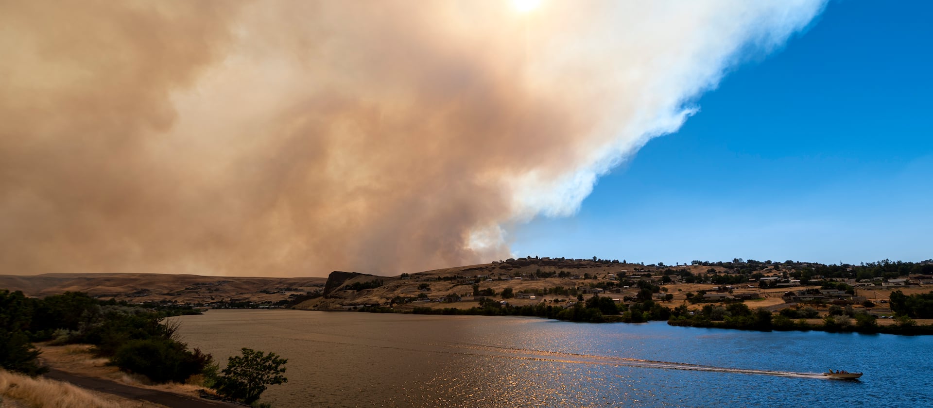 A boat heads down the Snake River as smoke from a fire west of Clarkston, Wash., wafts eastward into Lewiston, Idaho.