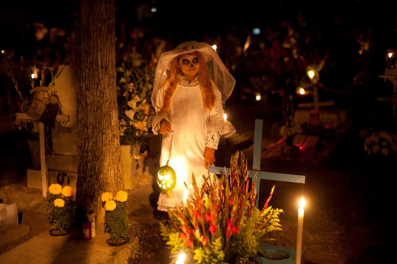 Frangerato Salvador, 8, dressed as a Katarina, stands beside her brother's grave, marking the Day of the Dead holiday at the cemetery in San Gregorio, Mexico, Thursday, Nov. 1, 2012. The holiday honors the dead on Nov. 1, coinciding with All Saints Day an