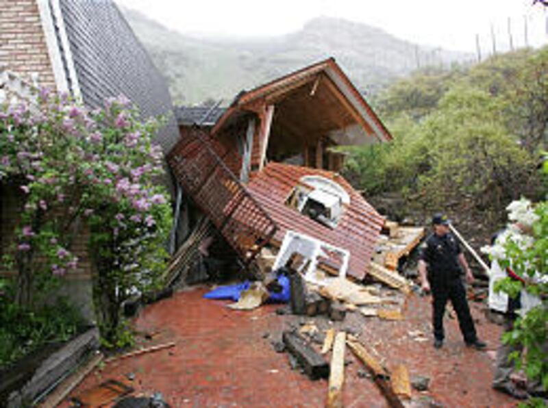 A Provo police officer stands in front of a home damaged Thursday when a 6-by-7-foot boulder rolled down Y mountain.