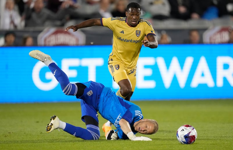Colorado Rapids goalkeeper William Yarbrough, wearing blue, tumbles to the pitch after stopping a shot by Real Salt Lake midfielder Anderson Julio