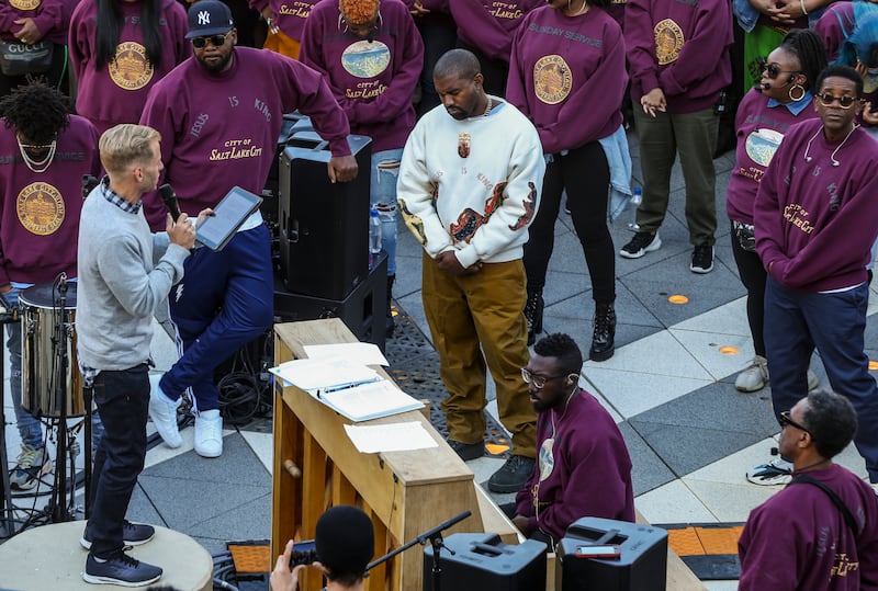 Kanye West, white sweater, bows his head in prayer during his “Sunday Service” at The Gateway in Salt Lake City on Saturday, Oct. 5, 2019. Thousands packed into the outdoor mall, causing people to stand on and climb up anything they could find to catch a glimpse of West.