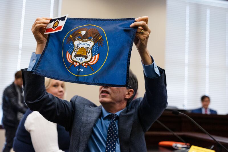Michael De Groote displays a small version of the proposed new Utah state flag against a larger version of the current flag during a meeting of the Utah Senate Business and Labor Committee to discuss a bill to change the state flag at the Capitol in Salt Lake City on Wednesday.