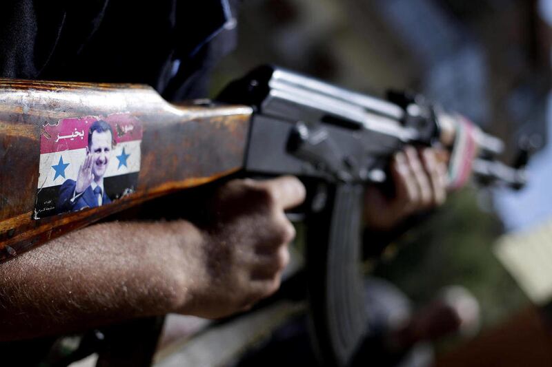 In this Wednesday, Aug. 21, 2013 file photo, a Syrian military soldier holds his AK-47 with a sticker of Syrian President Bashar Assad and Arabic that reads, "Syria is fine," as he stands guard at a check point on Baghdad street, in Damascus, Syria.