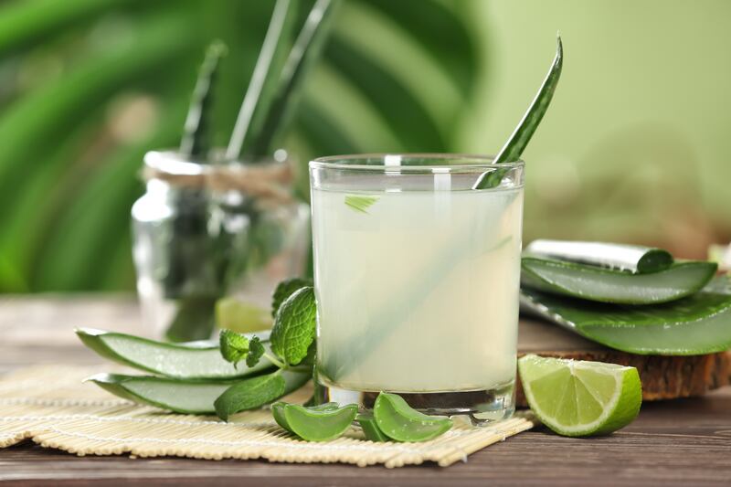 An aloe vera juice drink sits on a table surrounded by cut limes.