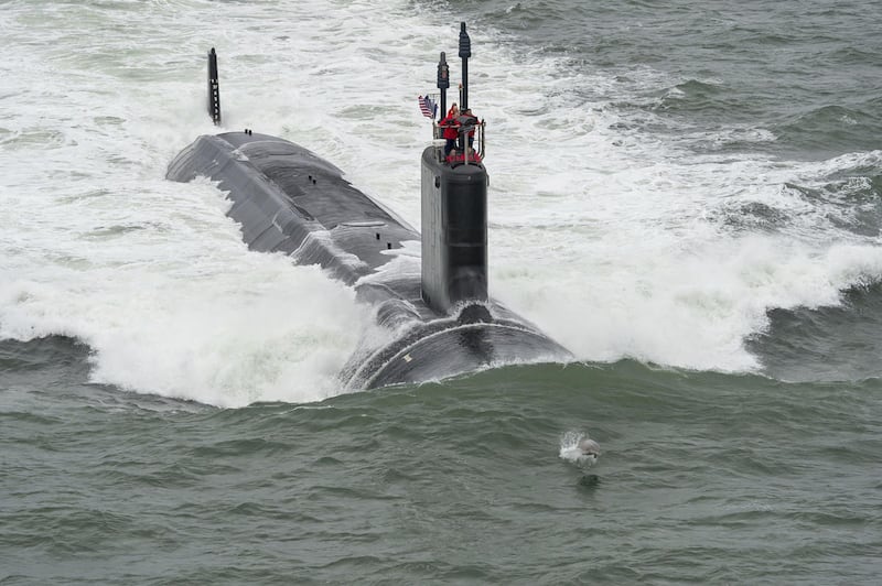 This Thursday May 21, 2015 photo provided by Huntington Ingalls Industries shows the Virginia-class submarine USS John Warner (SSN 785) as a dolphin jumps in the bow wave as it conducts sea trials off the Virginia Coast.