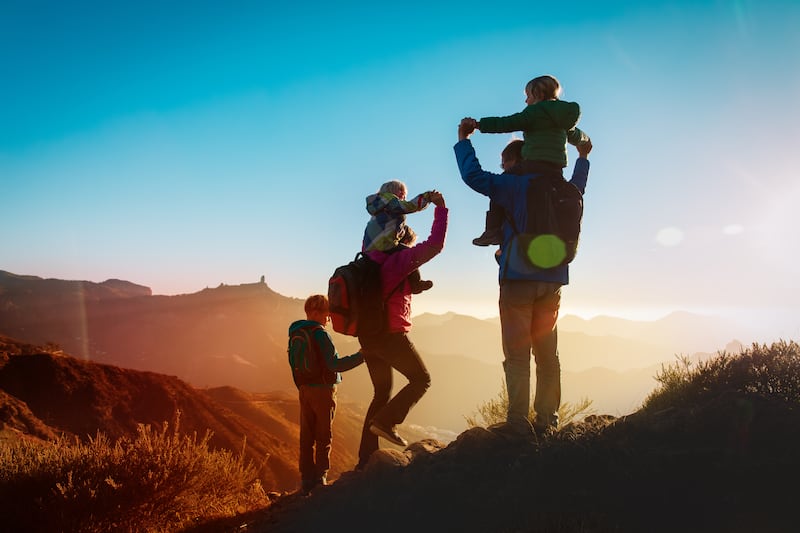 Family with three kids hike in the mountains at sunset.