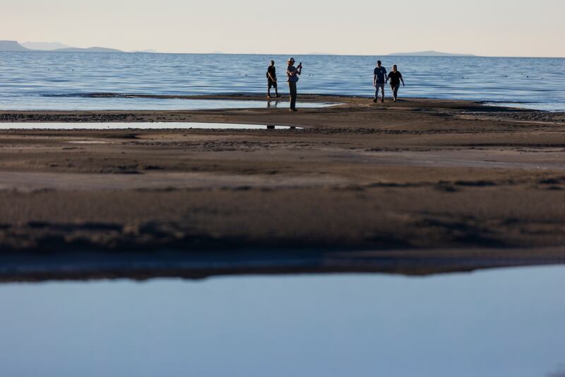 Kevin Sullivan watches as Martha Sullivantakes a photo while Kevin Sullivan holds the hand of his girlfriend, Linnea Scott, as they walk the shore of the Great Salt Lake.
