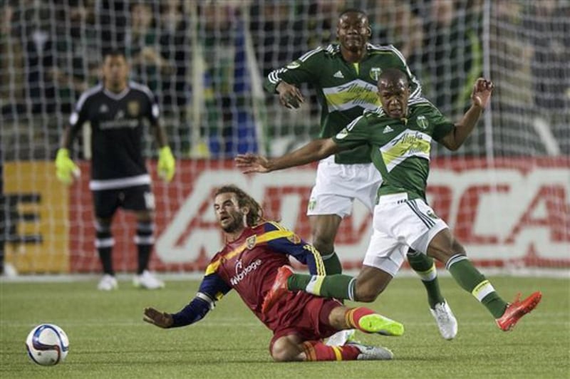 Kyle Beckerman, lower left, of Real Salt Lake, slide tackles Darlington Nagbe, right, of the Portland Timbers, during the first half of an MLS soccer game, Saturday, March 7, 2015, in Portland, Ore.