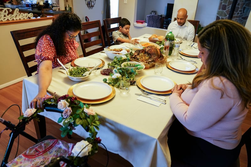 Vivian Zayas holds onto the walker once belonging to her recently deceased mother Ana Martinez while her family prays before Thanksgiving dinner, Thursday, Nov. 26, 2020, in Deer Park, N.Y. Members of President Joe Biden’s COVID-19 response team fear herd immunity won’t come until Thanksgiving 2021.