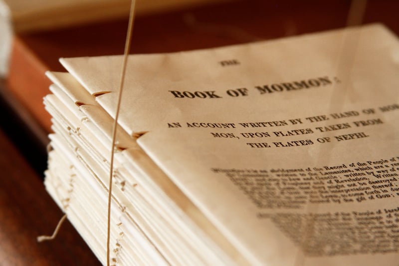 Folios of pages of a first-edition Book of Mormon are shown as binding string stitches them together into a finished book.
