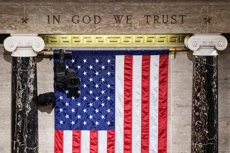 “In God We Trust” is engraved in stone above a U.S. flag in the House of Representatives chamber at the Capitol in Washington.