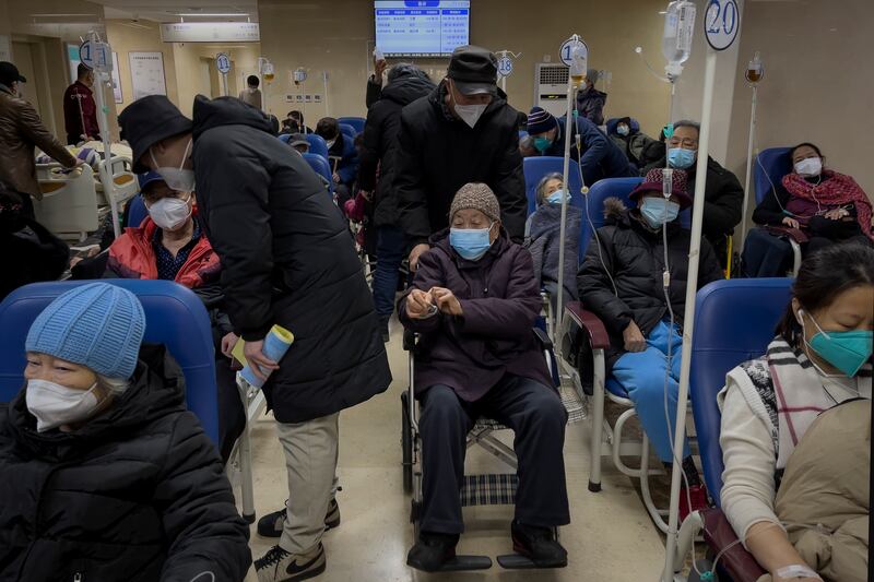 A man pushes an elderly woman past patients receiving intravenous drips in the emergency ward of a hospital, Jan. 3, 2023.