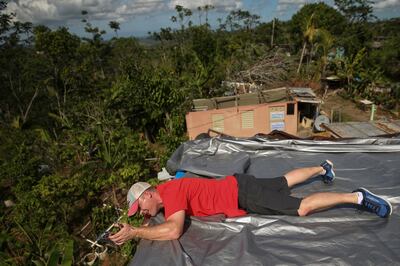 Dan Dustin installs a new tarp on Aida Noemi Valentin Ramos' leaking roof in Furnias Barrio, Puerto Rico, on Sunday, Dec. 10, 2017.