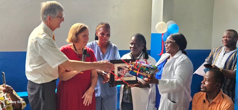 A senior missionary couple presents gifts to Eleanor K. Sampsonthe, the officer in charge of the Soniwein Health Center, during the Dec. 27, 2025, ceremony celebrating the recently renovated health center in Monrovia, Liberia.