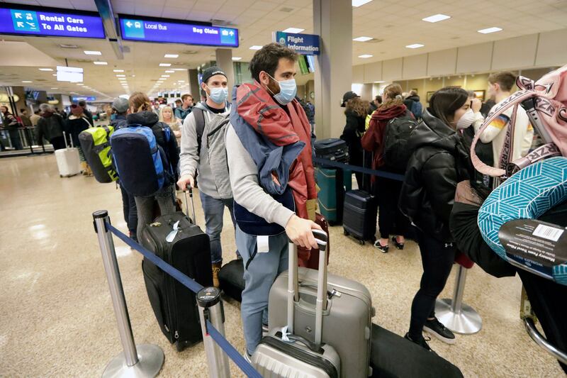 Masked travelers stand in line with luggage before getting to the ticket counter at the Salt Lake City International Airport Sunday, March 15, 2020, in Salt Lake City.