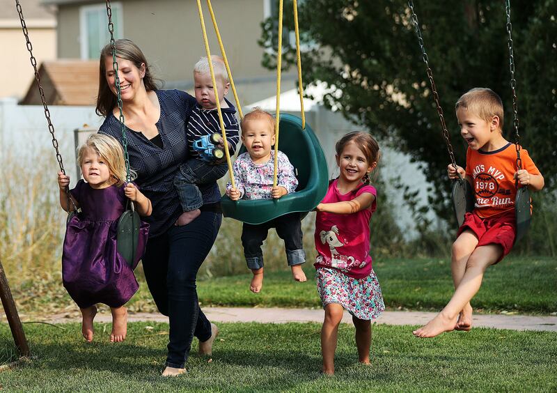 Lisa Draper, a member of Momni, holds her son Derek and plays on the swings with her children and two of Kelsey Atherton's children in Lehi on Saturday, Aug. 18, 2018.