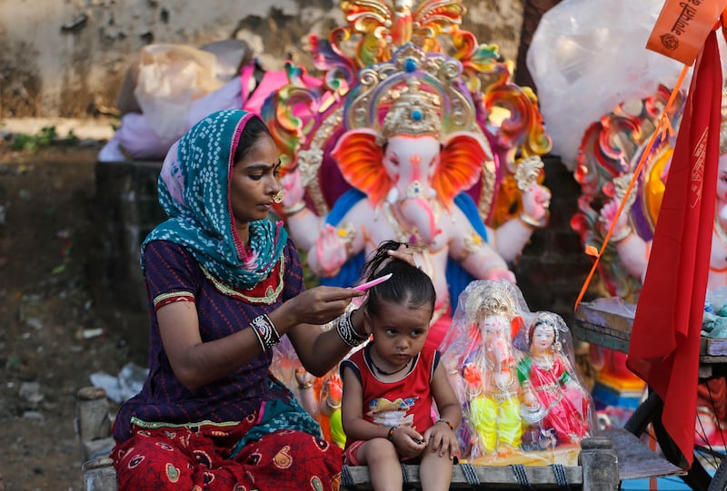 An Indian woman combs the hair of a child as she waits for customers for idols ahead of Ganesh Chaturthi festival in India.