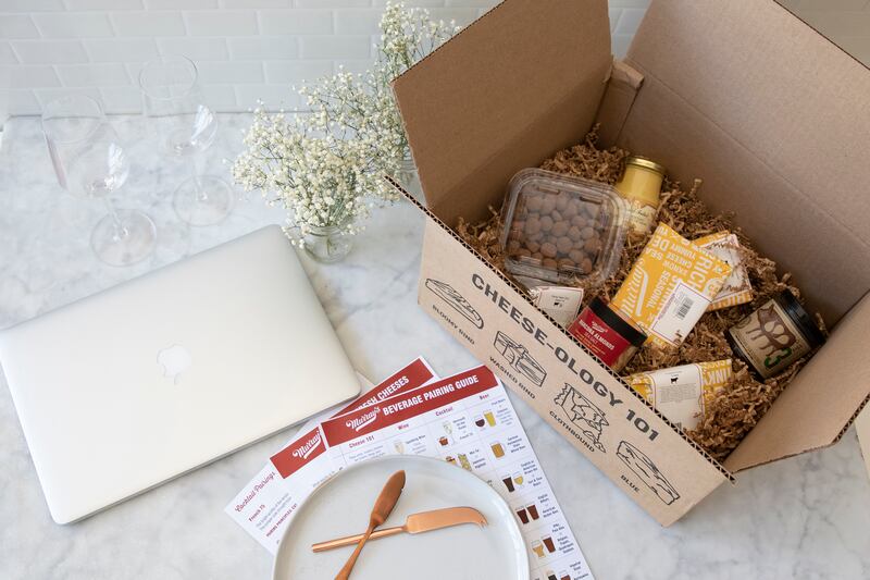 This image released by Murray’s Cheese shows a box filled with cheeses and other pairings by a laptop for a virtual class about cheese.