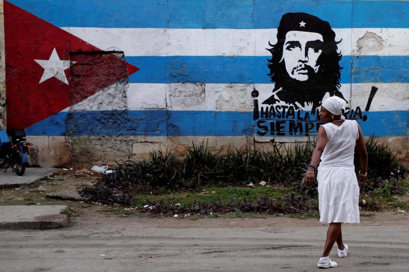 A santera looks back while crossing the street where a wall is covered with a mural of the Cuban flag and an image of Cuba's revolutionary hero Ernesto "Che" Guevara in Havana, Cuba, Friday Jan. 27, 2012. After economic reforms by President Raul Castro we