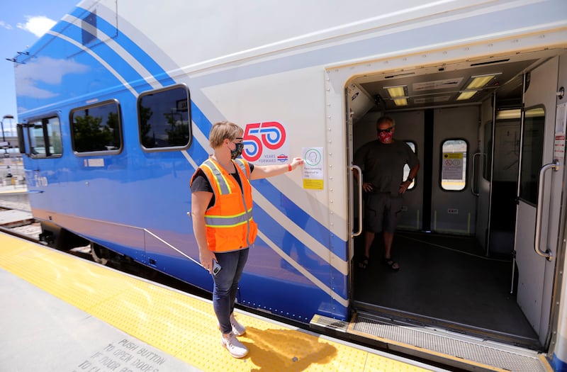 Marci Warren, Utah Transit Authority customer experience researcher, holds a sign up to a FrontRunner train at the Salt Lake Central Station in Salt Lake City on Wednesday, July 1, 2020, as she and her team test where to hang new signs alerting passengers that face masks must be worn in order to ride public transit.