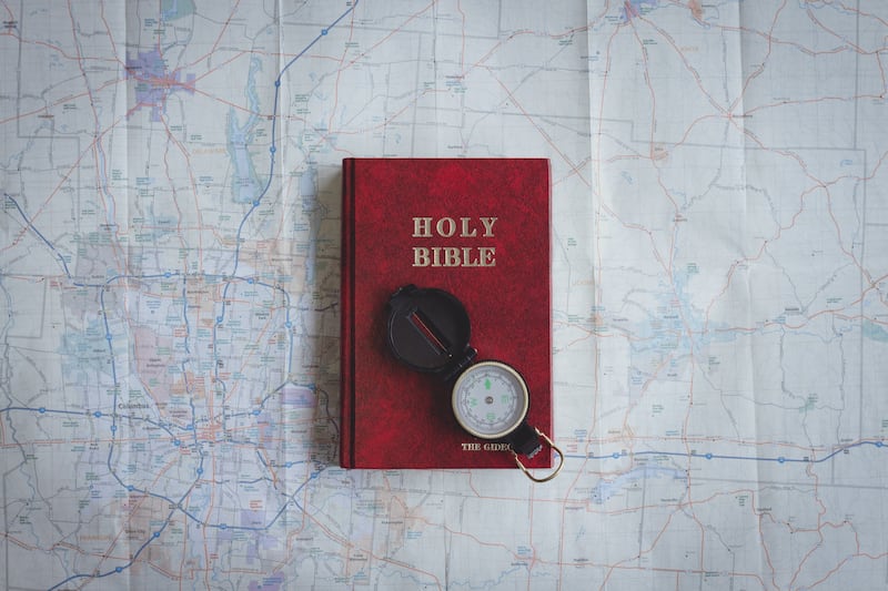 A red copy of the Bible sits on a map with a compass open on top.