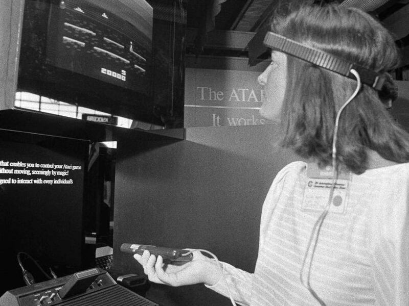 FILE- In this June 5, 1984, file photo, a woman in Chicago demonstrates Atari's new game, Mind Link, which utilizes a headband that picks up electrical impulse from the movement of the forehead and transmits them to a receiver attached to a video game or