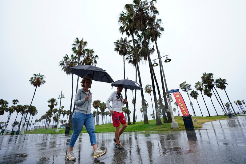 People walk along Venice Beach in the rain in Los Angeles.