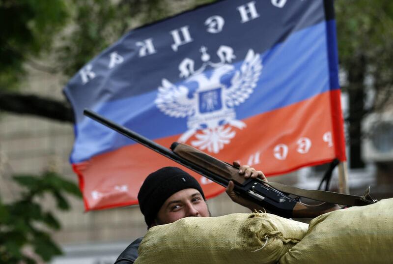 A pro-Russian gunman stands behind the barricades and shows his hunting rifle in front of the flag of the self-proclaimed Donetsk People's Republic, in the center of Slovyansk, eastern Ukraine, Thursday, May 8, 2014.