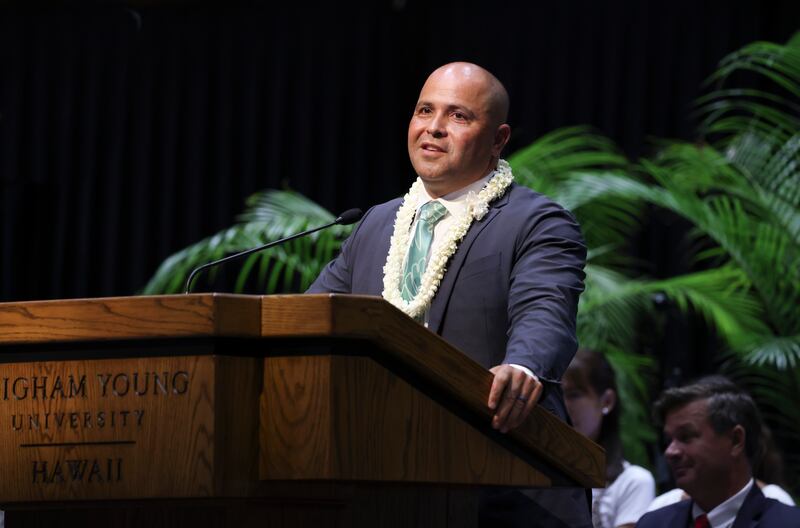 BYU–Hawaii President John S.K. Kauwe III wearing flower leis and speaking at a pulpit.