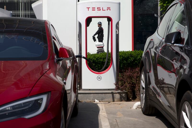 In this April 14, 2017, file photo, a security guard moves past Tesla electric vehicle charging station in Beijing. More than 200 manufacturers, including Tesla, Volkswagen, BMW, Daimler, Ford, General Motors, Nissan, Mitsubishi and U.S.-listed electric v