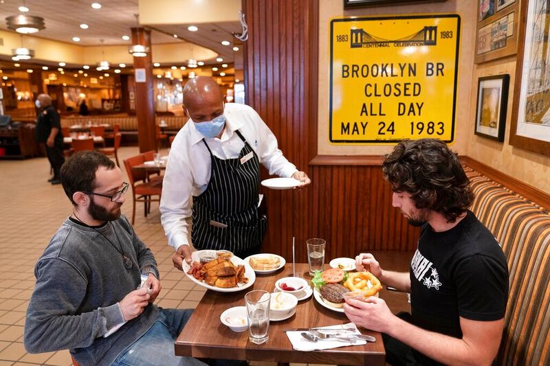 Waiter Lenworth Thompson serves lunch to David Zennario, left, and Alex Ecklin at Junior’s Restaurant in New York in 2020.