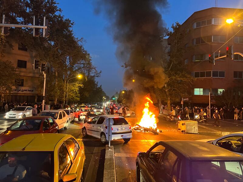 A police motorcycle burns in the middle of the street surrounded by cars and smoke.