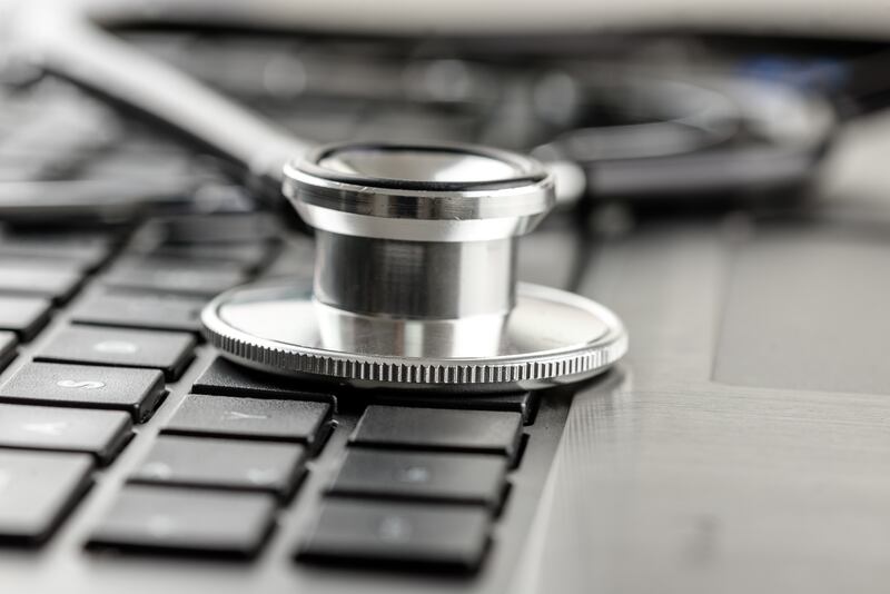 Close up of the silver metal disk of a medical stethoscope on a laptop keyboard.
