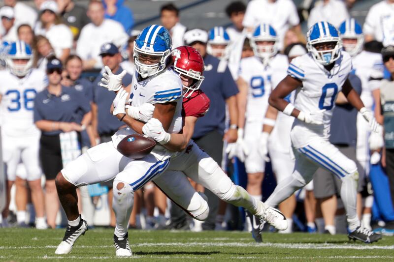 Keanu Hill (wearing white), a wide receiver for the BYU Cougars, drops a pass during a tackle from Drew Sanders
