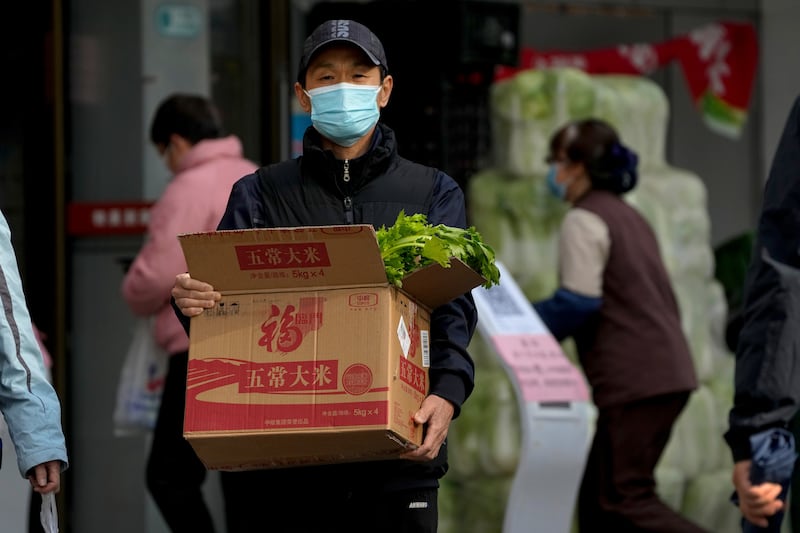 A man wearing a face mask carries a box with groceries as he leaves a supermarket in Beijing on Sunday, Nov. 27, 2022.