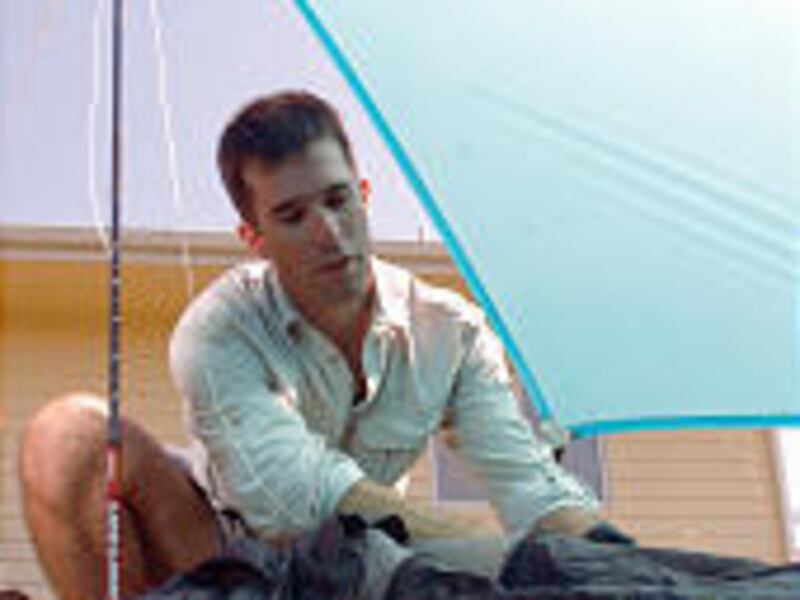 Ryan Jordan of Bozeman, Mont., looks over a sleeping bag under a tarp that doubles as a rain poncho. Jordan, who critiques lightweight backpacking equipment, recently hiked 225 miles with a 20-pound pack.