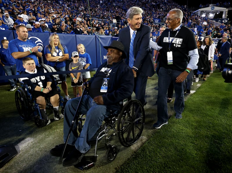 Elder S. Gifford Nielsen pushes Mel Hamilton’s wheelchair and talks with John Griffin, members of the 1969 Wyoming Black 14.