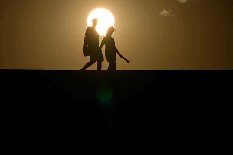People walk along a trail as the sun sets on July 16, 2023, in Death Valley National Park, Calif.