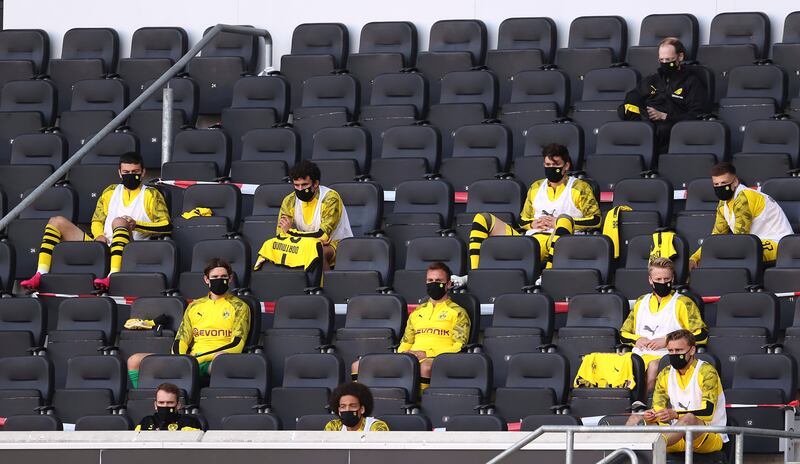 In this Sunday, May 31, 2020, substitutes for Borussia Dortmund, wearing face masks to protect against coronavirus, look on from the stands during the German Bundesliga soccer match between SC Paderborn 07 and Borussia Dortmund at Benteler Arena in Paderborn, Germany.
