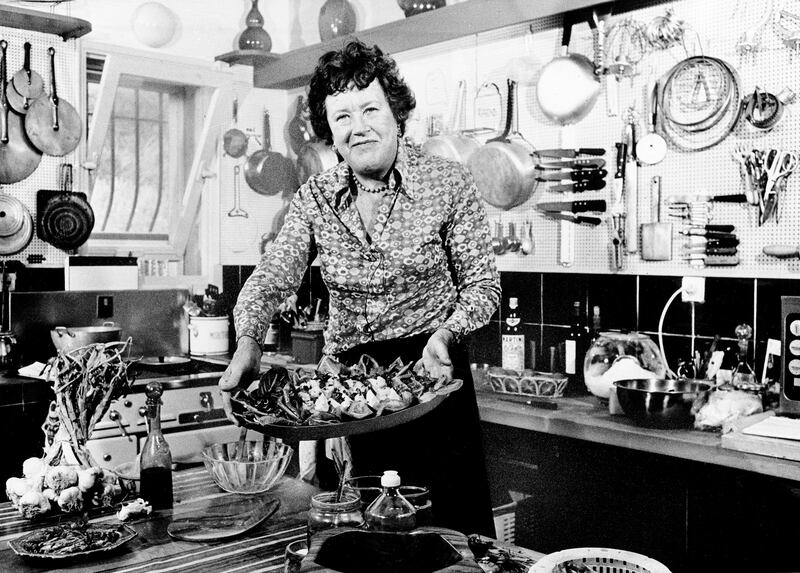 Julia Childs holds up aplatter of salade nicoise in her kitchen.