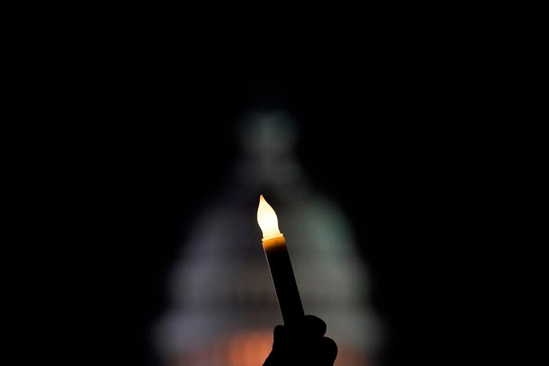 With the U.S. Capitol in the background, a person holds a candle at a vigil on the one-year anniversary of the Capitol attack.