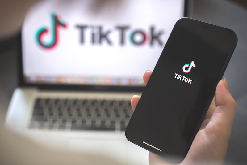 The TikTok logo is displayed on a phone screen and on a computer screen.