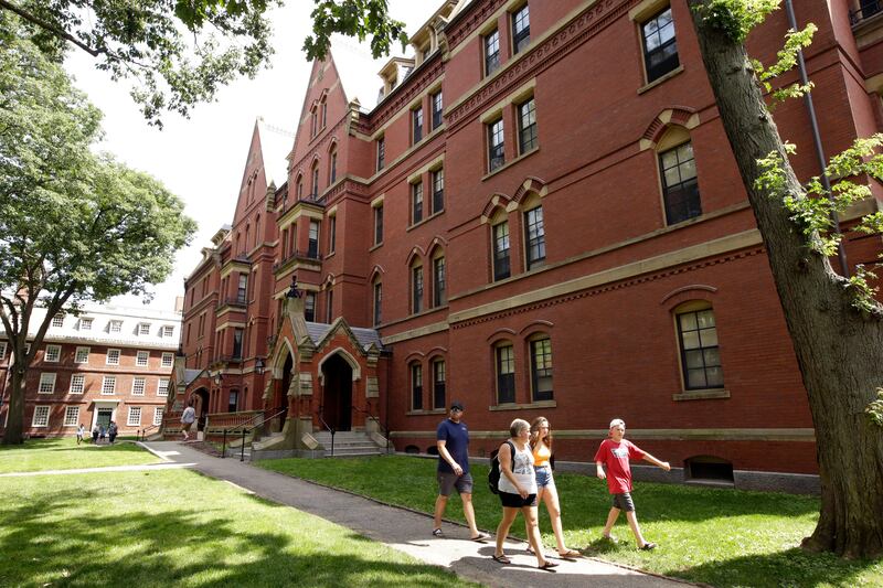 People walk along a sidewalk on the campus of Harvard University.