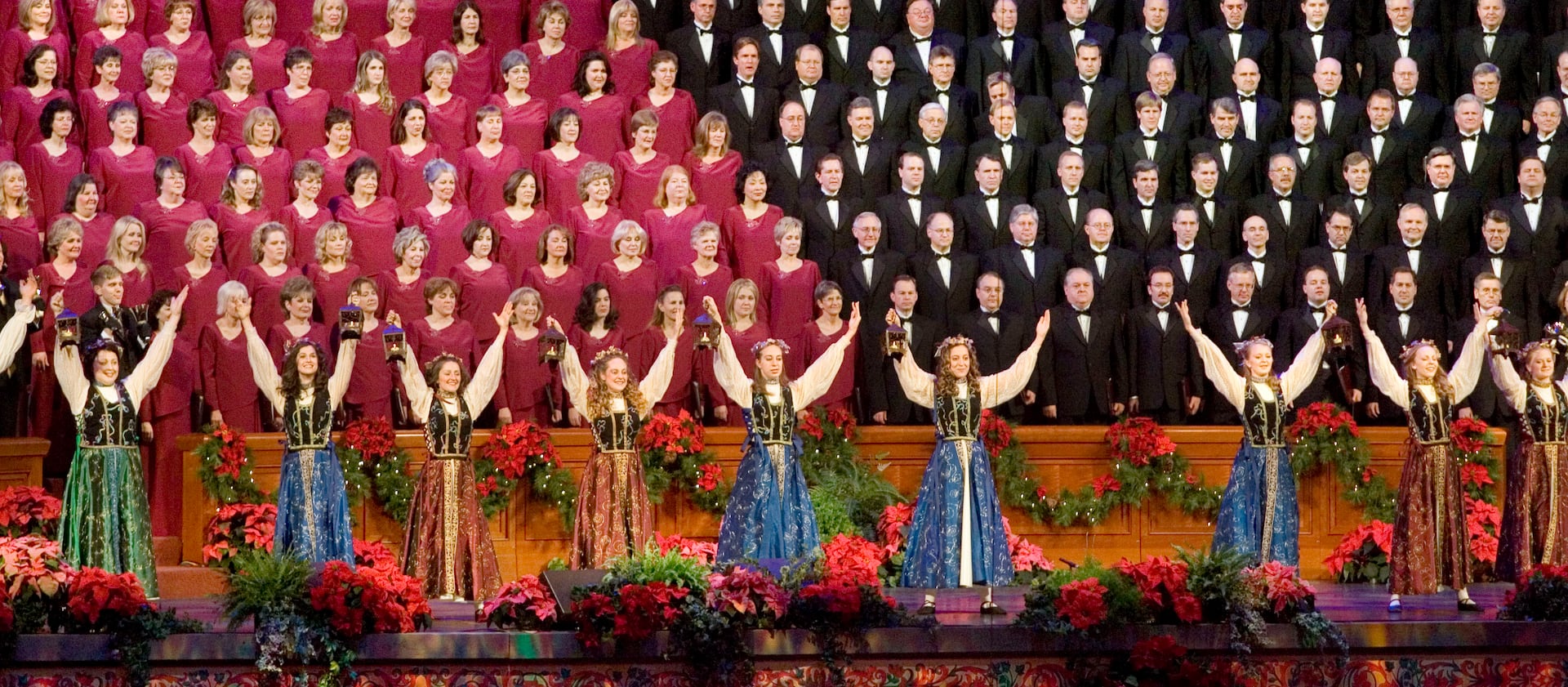 Dancers wearing costumes raise their arms in front of the Tabernacle Choir at Temple Square as they entertain the audience at the Conference Center during the Christmas concert in Salt Lake City.