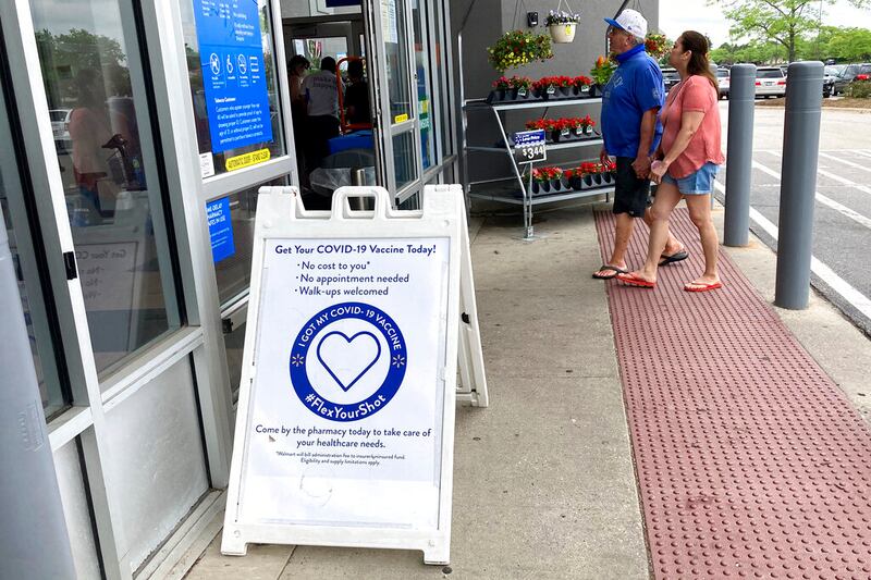A covA COVID-19 vaccine information sign is seen as shoppers walk in a Walmart store without masks in Vernon Hills, Ill.