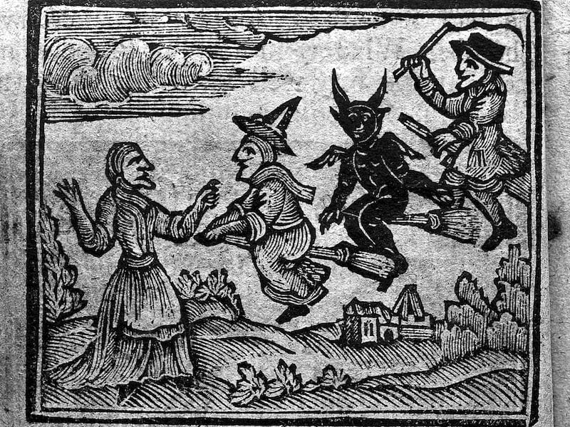 Witches flying on broomsticks in front of a house.